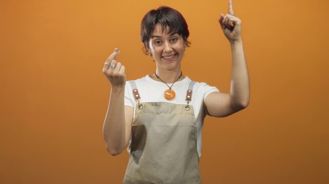 Woman jeweler wearing apron holding a ring between fingers and pointing up in a studio; cheerful craft pride.