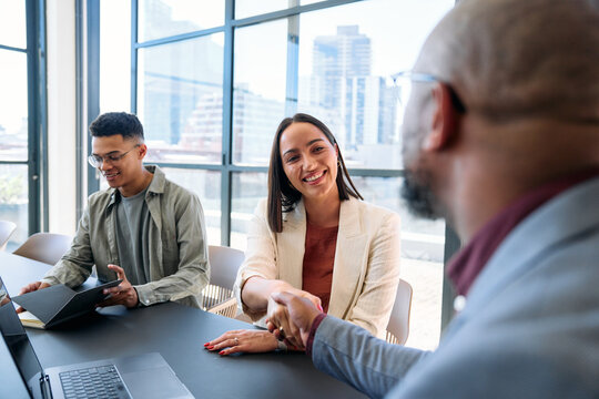 Smiling young businesswoman shaking hands with colleague in boardroom at office during daytime