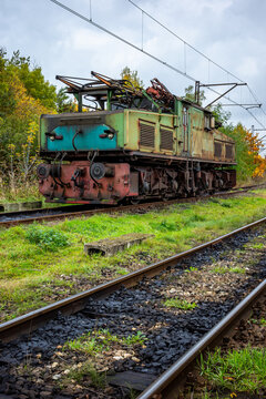 An old, green, electric shunting locomotive standing on a side track. The photo was taken on a cloudy autumn day.