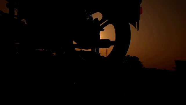 Silhouette of a motorcycle against a golden sunset sky with palm trees in the background. Cinematic outdoor scene representing travel, freedom, and adventure on Indian roads.