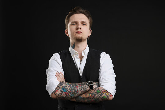Young man with tattoos in stylish vest and shirt on black background