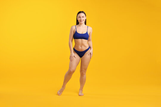 Beautiful woman in stylish swimsuit posing on yellow background