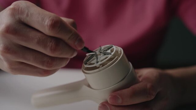 Closeup hands cleaning blades of modern electric lint remover with specialized small brush, performing routine maintenance on household appliance for clothing care. Shooting in slow motion.