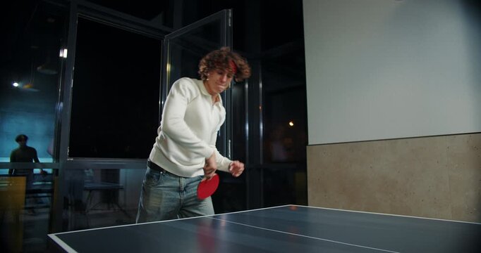 Man returning shot in table tennis game indoors at night