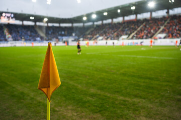 Yellow corner flag on a green grass soccer pitch with a blurred view of a professional stadium and crowd in the background. © Dziurek