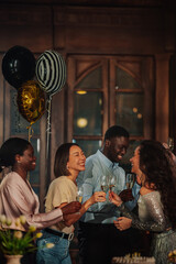 Fototapeta premium Diverse friends celebrating a party, toasting with champagne glasses and laughing. Joyful social gathering with balloons