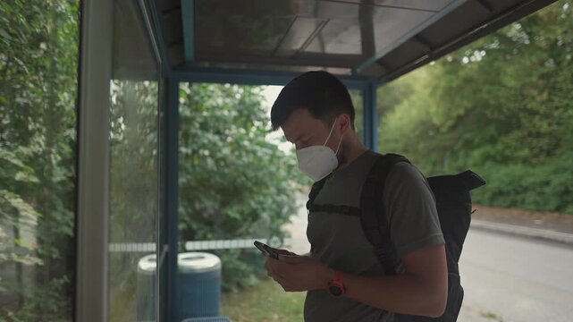 Man wearing face mask checks bus timetable and route map at a bus stop in Trudering, Munich, Germany. Summer public transport scene with urban commuting, travel planning and seasonal pollen allergy.