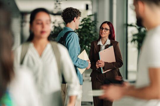 Professor talking with a young male student in a modern university hallway, discussing education and learning