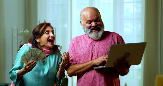 Senior Indian couple holding a five hundred rupee money fan with a laptop, looking surprised and joyful while cash is raining from above to denote sudden growth