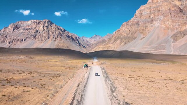 Drone following a vehicle navigating a rough dirt road and infrastructure repair zone in Spiti Himalayan valley.