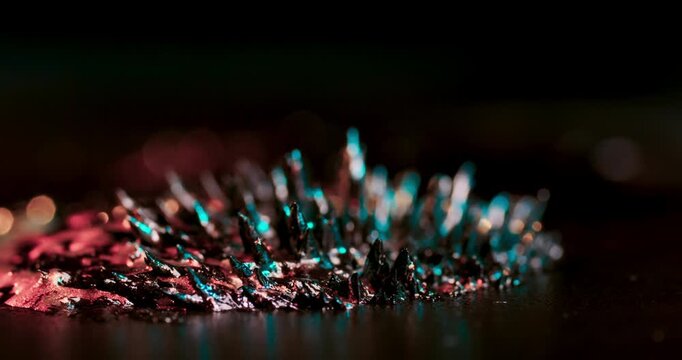 Watch shimmering metal particles react to a magnet against a black background. This dynamic scene is perfect for stunning motion graphics and visual effects that captivate the audience