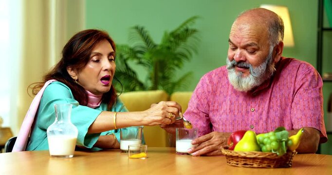 Senior Indian couple sitting at a breakfast table in their modern home, drinking healthy turmeric milk, also known as haldi or golden milk, for wellness