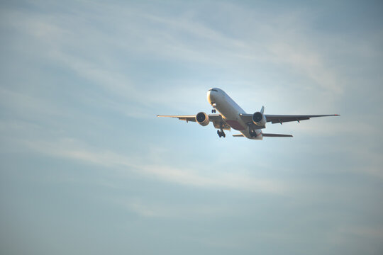 Front view of a twin-engine passenger airplane on final descent with landing gear down, flying through a soft clouded sky, suitable for aviation, travel, and global transportation themes.