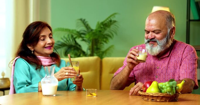Senior Indian couple sitting at a breakfast table in their modern home, drinking healthy turmeric milk, also known as haldi or golden milk, for wellness