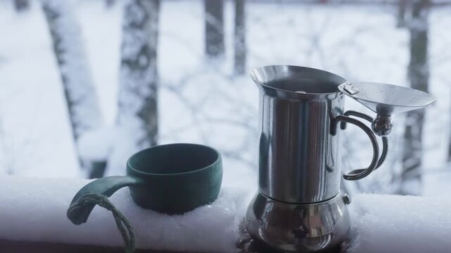 A cozy coffee pot rests on a snowy balcony, inviting warmth as the soft white landscape glistens in the morning light.