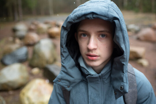 portrait of a teenage boy in a hooded jacket outdoors in a forest park on a snowy day.