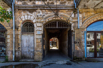 Fototapeta premium Classic architecture of an old brick building facade in Sukhum with an arched driveway and ornate decorations. Weathered wooden doors and vintage iron gates on a sunny spring day. Abkhazia.