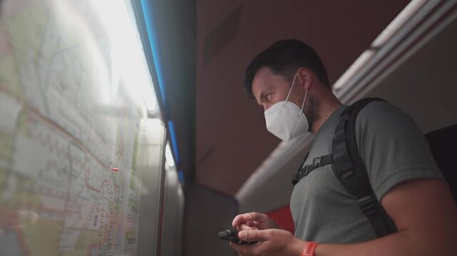 Male passenger with a weak immune system wearing a protective mask in the metro. He is planning his journey via smartphone due to train cancellations.