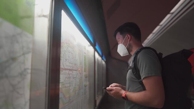 Man in a FFP2 mask at a Munich subway station checking the map and using his phone to find an alternative route during a transport strike in Germany.
