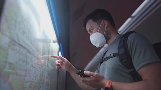 Patient man in a mask navigating the Munich underground. He uses his phone to check the schedule after a massive transport strike announcement. Using mobile app to navigate public transport 