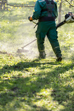 Landscaper cutting overgrown grass with brush cutter in park