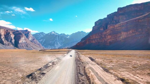Low-altitude aerial view of an off-road vehicle navigating the rugged, barren valley floor of Spiti, India.
