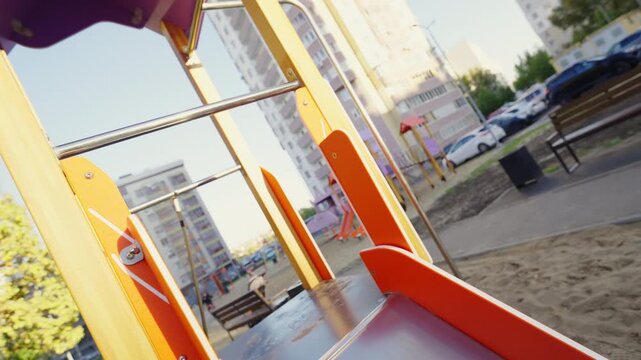 Orange slide extends from play tower below purple roof in courtyard. Smooth chute leads from platform framing children play zone on sand