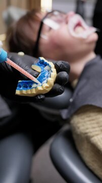 Close-up of dentist working with dental cast and impression material for crown planning. Prosthetic dentistry and teeth restoration process in clinic. Vertical video.