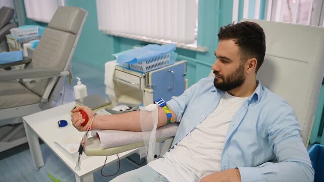 Male blood donor squeezing stress ball in hospital chair