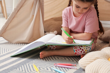 Little girl drawing in sketchbook near toy wigwam at home, closeup © New Africa