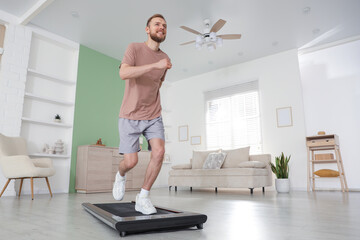 Fototapeta premium Sporty man training on treadmill at home, low angle view. Space for text
