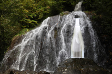 Obraz premium Pure water. Bottle against beautiful view on waterfall