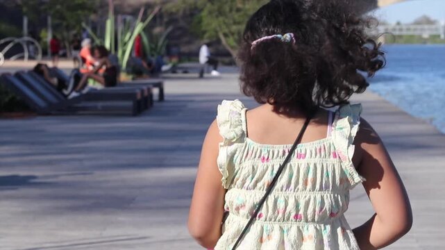 Little girl with curly hair running along a riverfront
