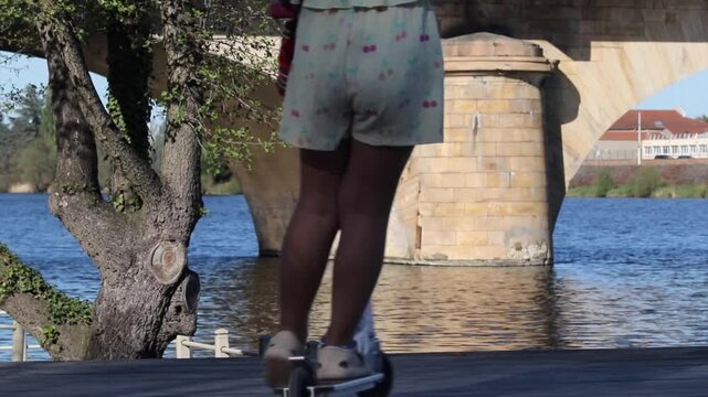 Girl riding a kick scooter on a riverside promenade