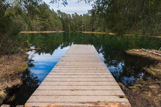 Wooden pier over the crystal clear turquoise water of Antu Sinijarv lake, the clearest lake in Estonia, surrounded by forest.