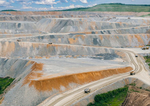 Terraced mine slopes with haul trucks on dirt roads, mining diamond and golden ore