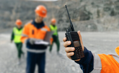 Worker holding walkie talkie with crew at open pit quarry