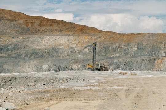 Drilling rig operating in large open pit mine landscape, gold mining industry