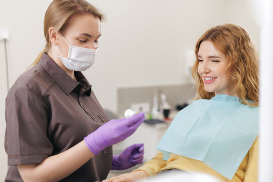 Female dentist showing mold to young caucasian female patient in dental clinic
