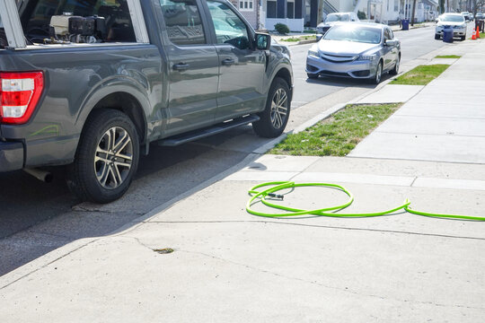 Pickup truck parked the wrong way on a street with a green kinked hose on the sidewalk