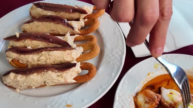 Hand serving traditional Spanish marineras with anchovy on bread rounds and octopus tapas on white plate in authentic Mediterranean restaurant setting