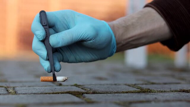 Forensic investigator in gloves collecting cigarette butt with tweezers at crime scene. Criminal investigation, evidence collection, police work concept. Close up.