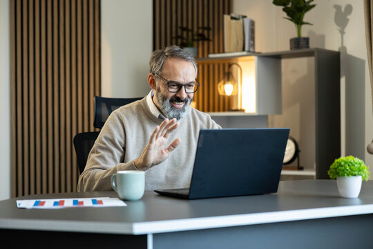 Smiling man connecting remotely from home office, participating in a virtual meeting using a laptop computer