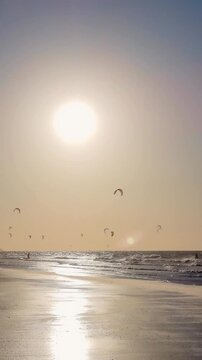 Silhouettes of kitesurfers at sunset with warm golden tones and ocean reflections.