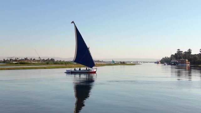 Peaceful view of a traditional felucca sailboat with a blue sail cruising on the calm waters of the nile river in luxor, egypt