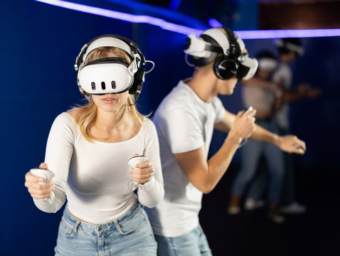 Young couple in VR glasses playing video game against another couple. Friends are enthusiastically playing a game in a virtual reality headset and using joysticks
