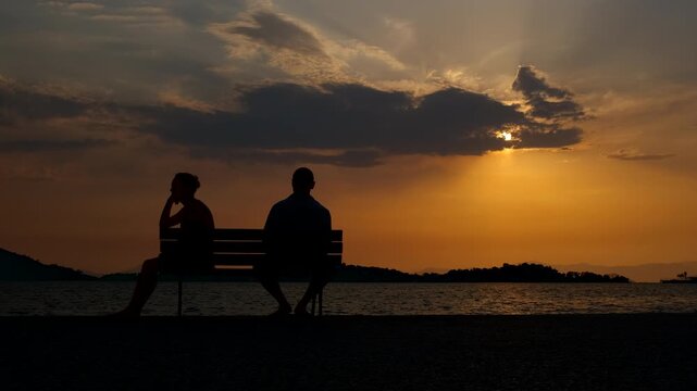 Man and woman think about problems in evening. A view of man sitting by woman back after quarrel against colorful dusk on the bay