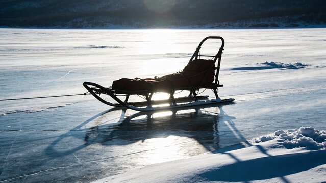 Winter Rescue Sled in Silhouette Across Frozen Lake with Windswept Snow and Low Sunlight