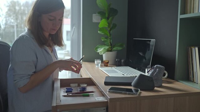 Woman opening desk drawer and taking stationery supplies at workspace