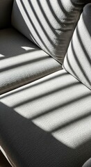 Geometric shadow patterns from window blinds fall across the textured upholstery of a modern grey fabric living room sofa.
